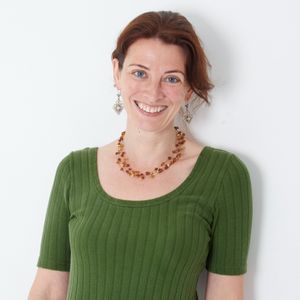 Kate Kingsford smiling. She has reddish brown hair and blue eyes. She is wearing a brown necklace and a green top